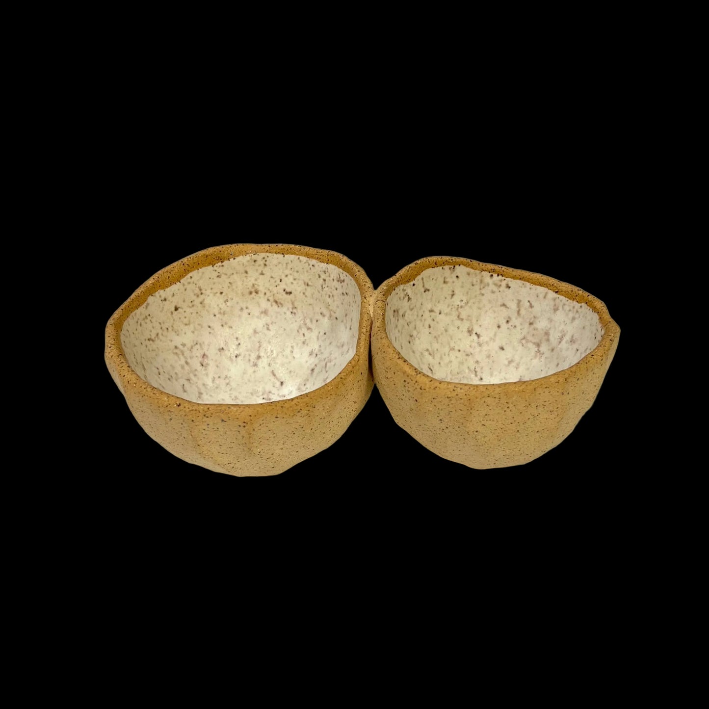 A pair of beige ceramic serving pods placed on a grey surface, designed for holding food items like nuts and dips.